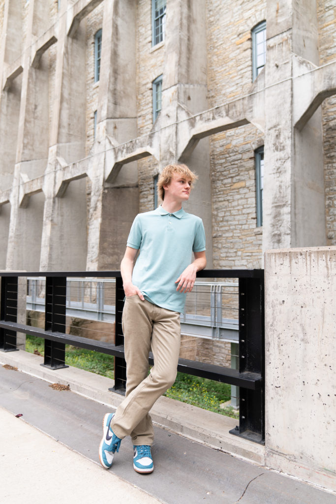 A high schools senior guy leans up against a railing during his senior pictures in front of the A-Mill Artist Lofts in Minneapolis, Minnesota