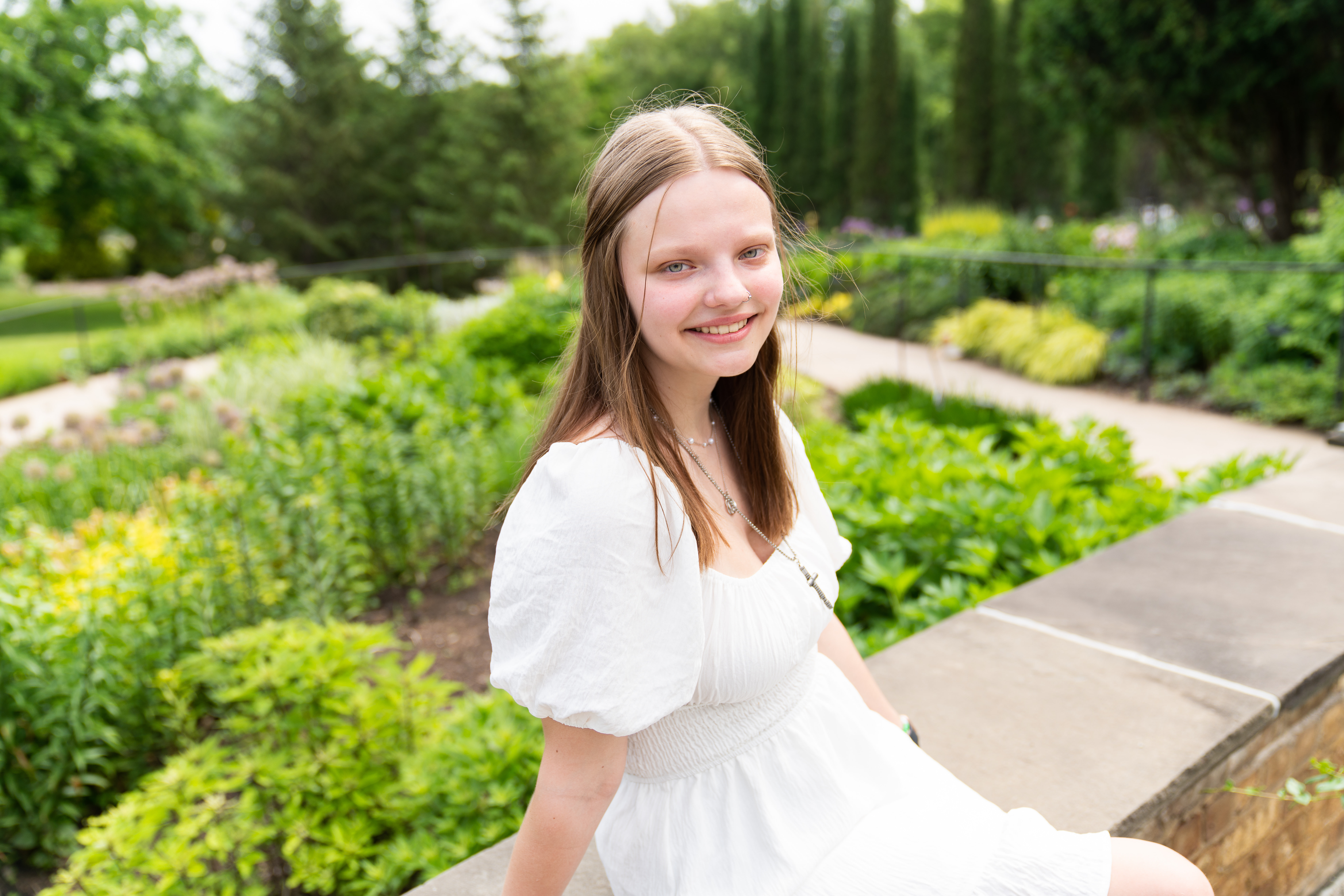 Teen girl wearing a white dress sits on a ledge for her senior photo.
