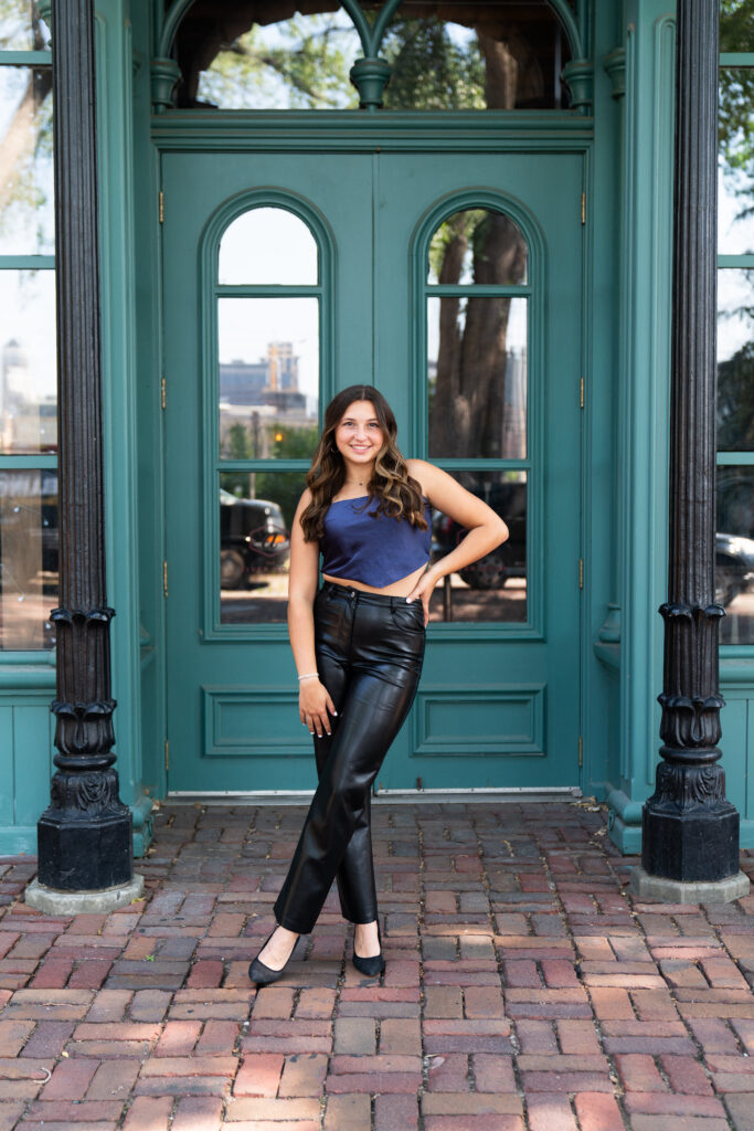 Girl poses for her senior pictures wearing leather pants and a satin top.