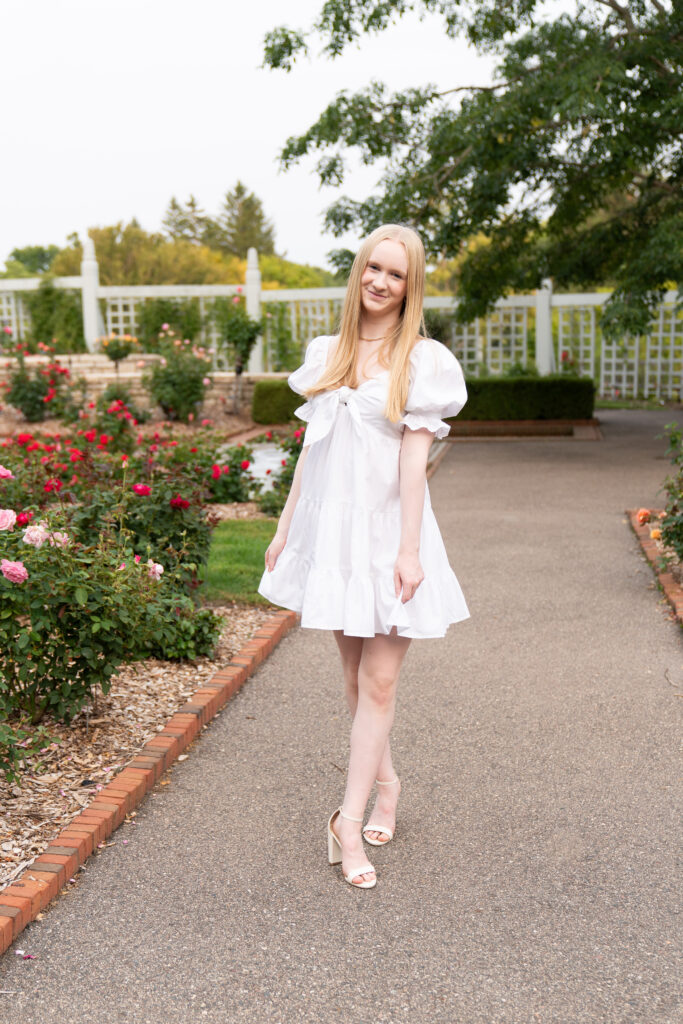 Girl walks toward the camera wearing a white dress for her senior pictures.