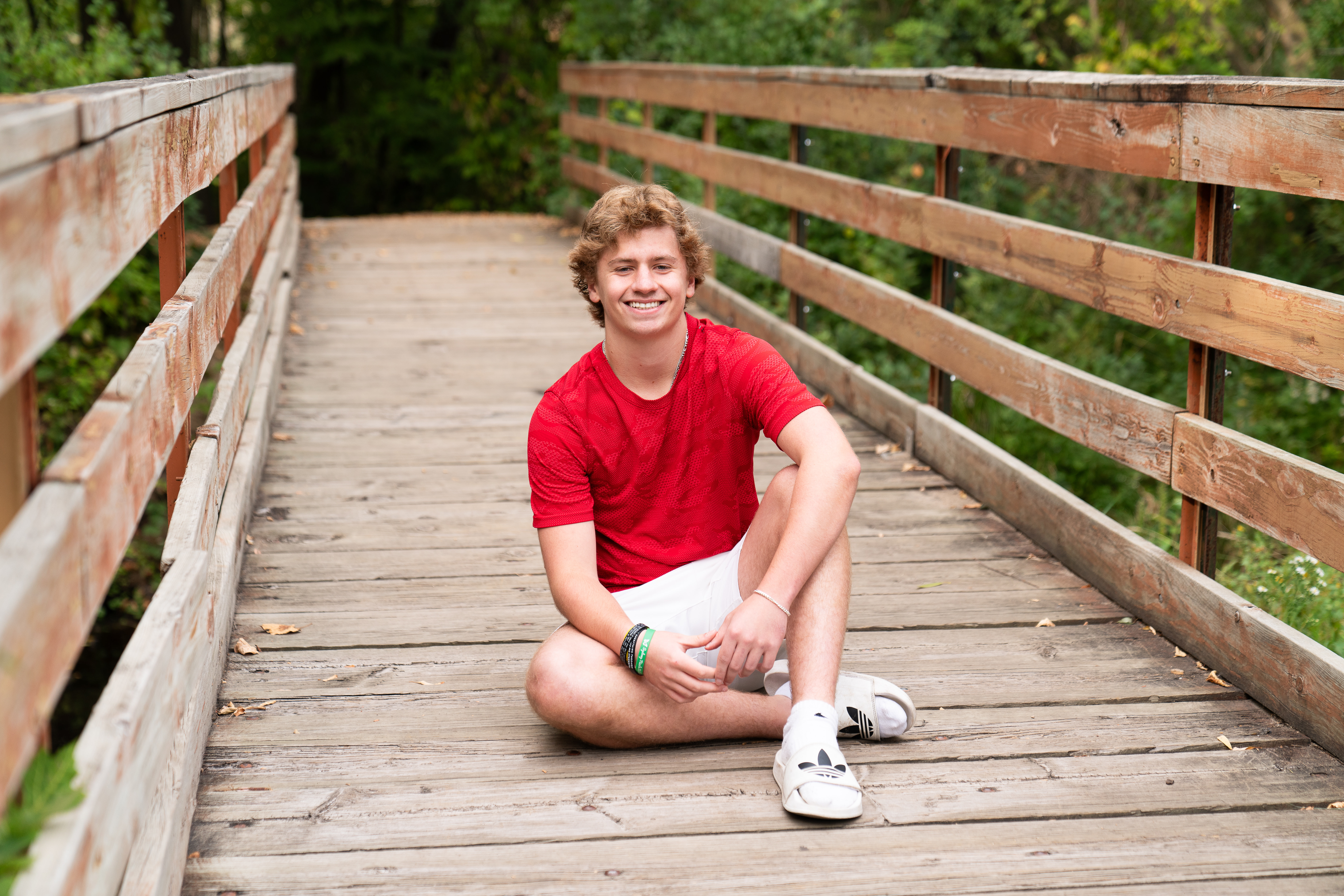High school aged guy sits on a bridge for his senior pictures at Hidden Valley Park in Savage, Minnesota.