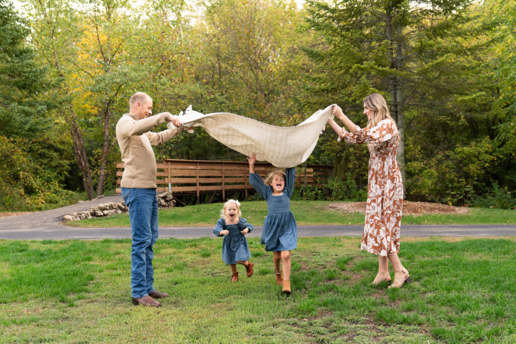 Two little girls run under a blanket that's being shaken by their mom and dad during their family photo session at Hidden Valley Park in Savage, Minnesota.