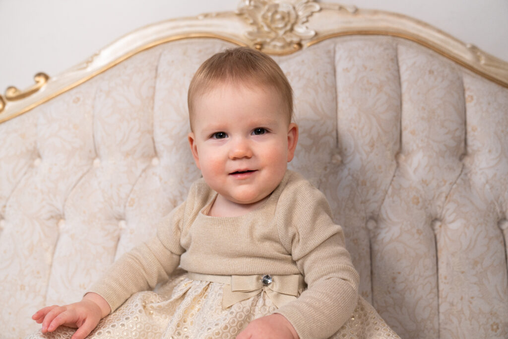 Little girl sitting on a victorian couch during her 1 year old pictures.