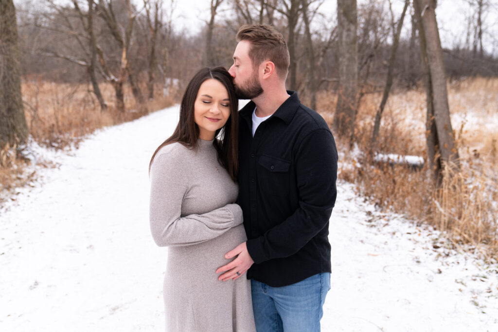 A man kisses his pregnant wife and holds her baby bump during their maternity photo session.