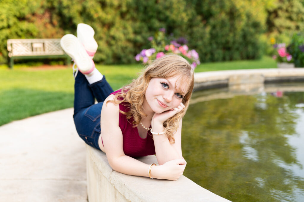 Teen girl poses on a fountain at Arneson Acres Park in Edina, Minnesota for her senior pictures.