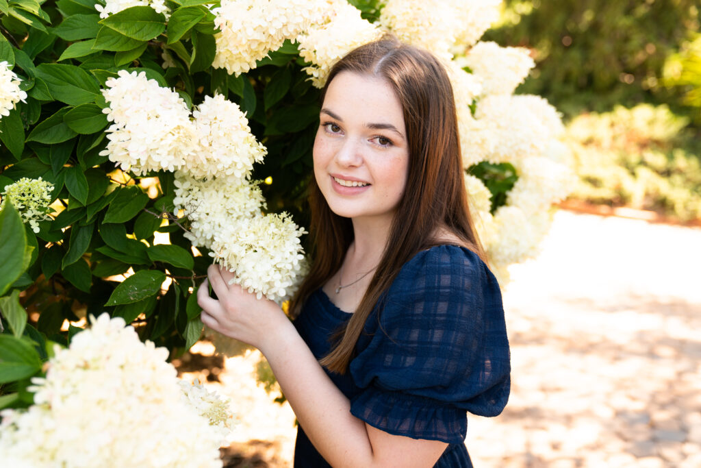 Senior girl posing next to a hydrangea tree for her summer senior photo shoot.