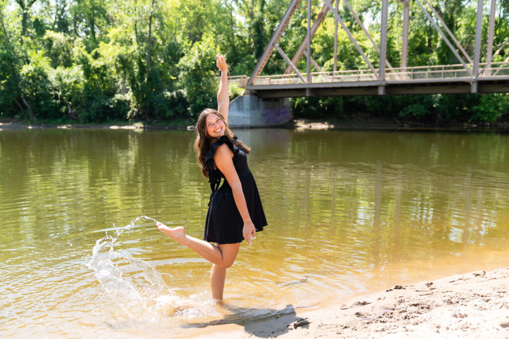 Senior girl plays in the water for one of her senior photo poses.