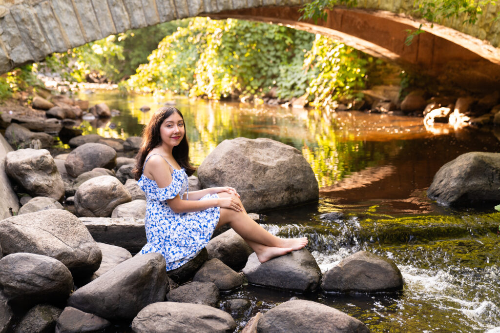 Senior girl sits on some rocks in the Minnehaha river in Minneapolis for her senior pictures.
