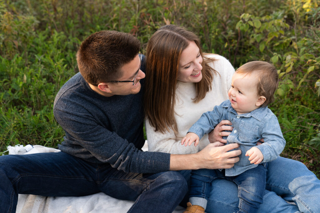 A mom and dad tickle their toddler during their family photo session at Lebanon Hills Regional Park in Eagan, Minnesota.
