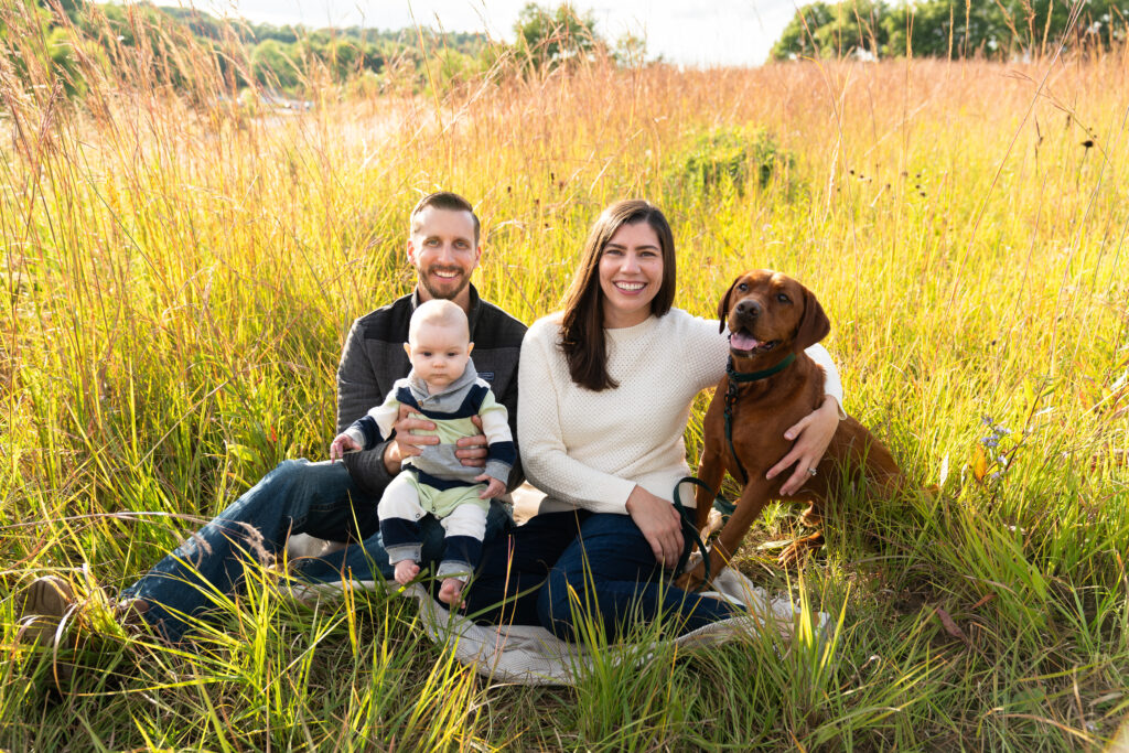 A family and their dog sit on a blanket in a field during their family photo shoot at Lebanon Hills Regional Park in Eagan, Minnesota.