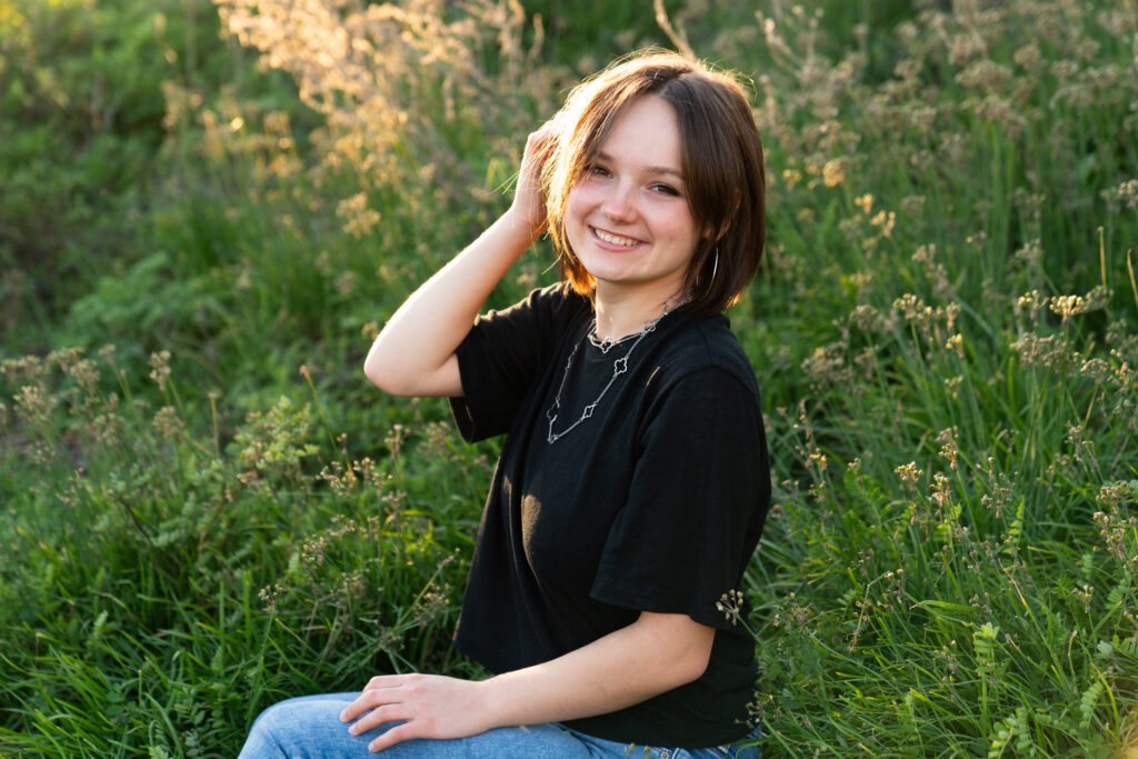 A girl plays with her hair in a field of grass during her senior photos.