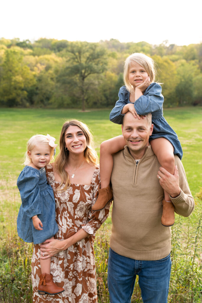 A family of four smiles at the camera during their fall family photo session at a park in Savage, Minnnesota.