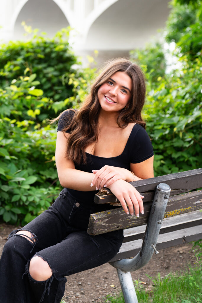 Girl sits on a bench and smiles at the camera during her senior picture photo shoot in Minneapolis, Minnesota.