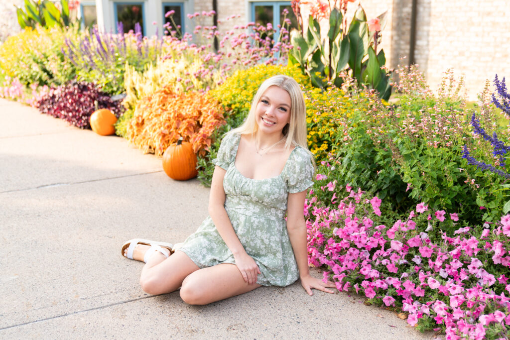 A girl sits on the ground next to flowers during her senior session.