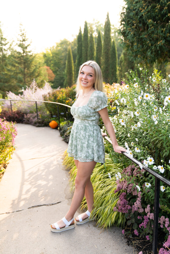 A high school teen girl poses next to some daisies during her senior session at the Minnesota Landscape Arboretum in Chaska, Minnesota.