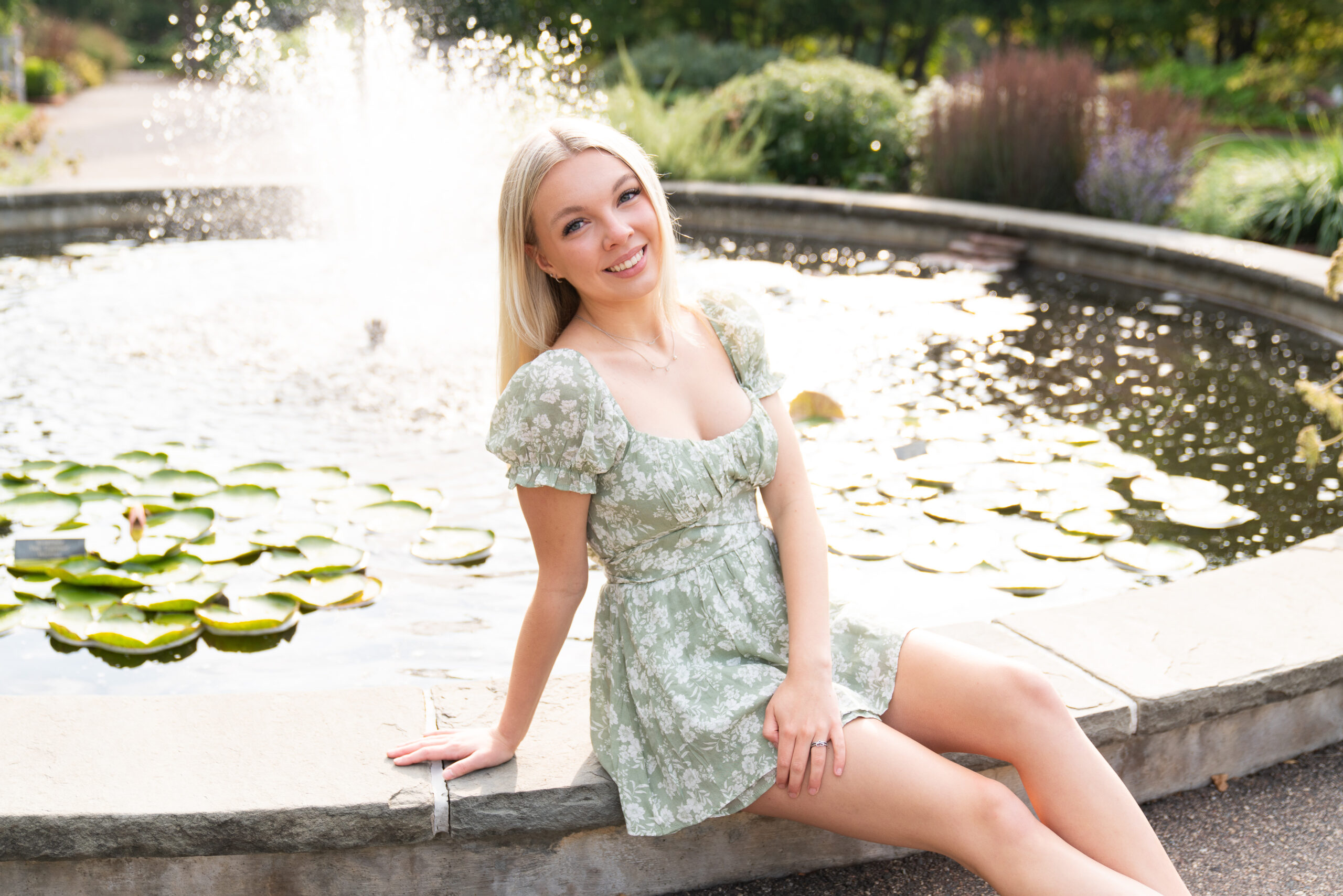 Girl sits next to a fountain during her senior session at the Minnesota Landscape Arboretum in Chaska, Minnesota.
