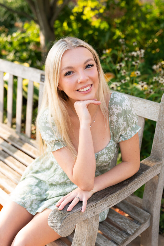 A teen girl sits on a bench and smiles at the camera for her senior pictures.