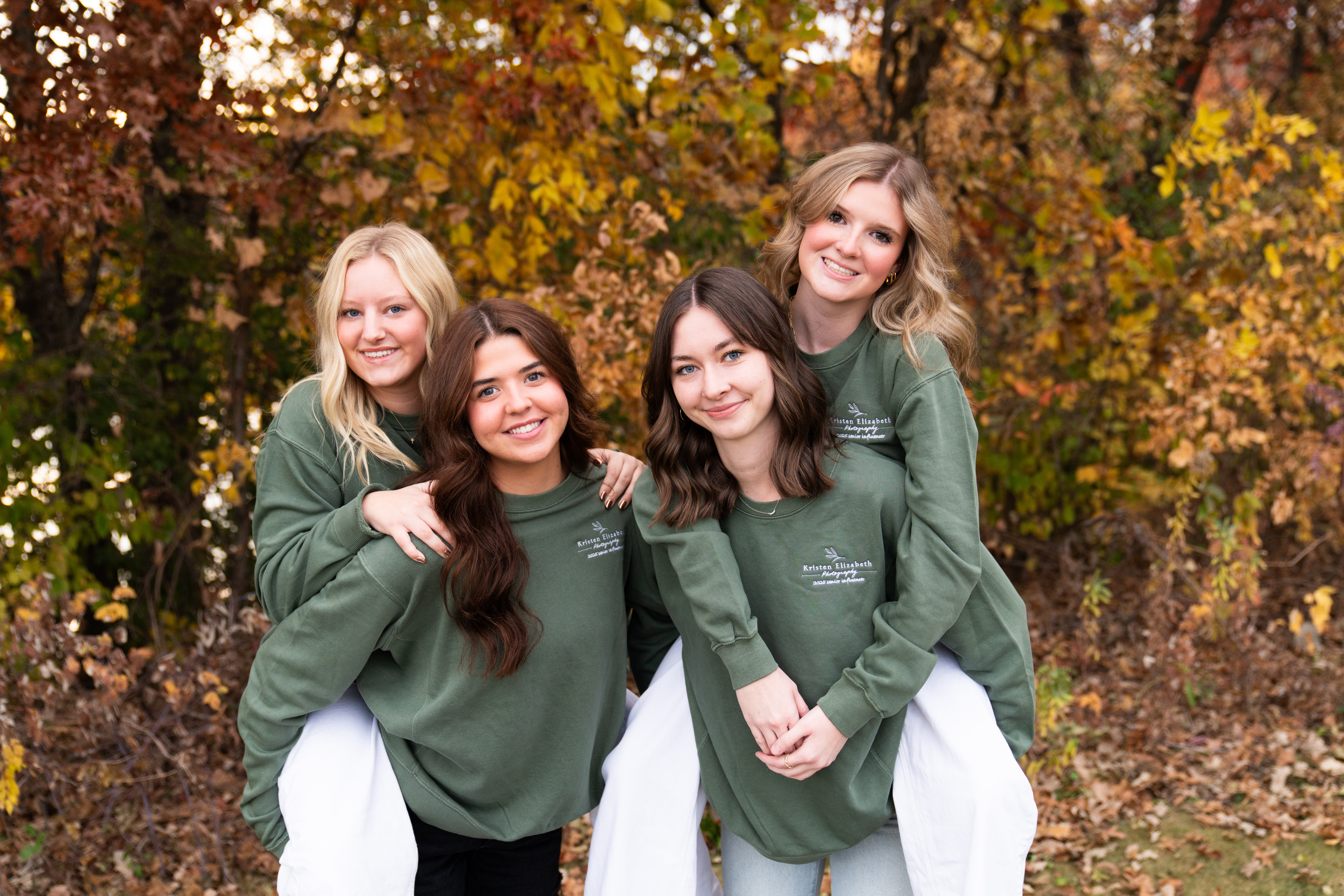 Four senior girls pose together, two girls giving the other two girls a piggy back ride for their fall senior rep team photo shoot.